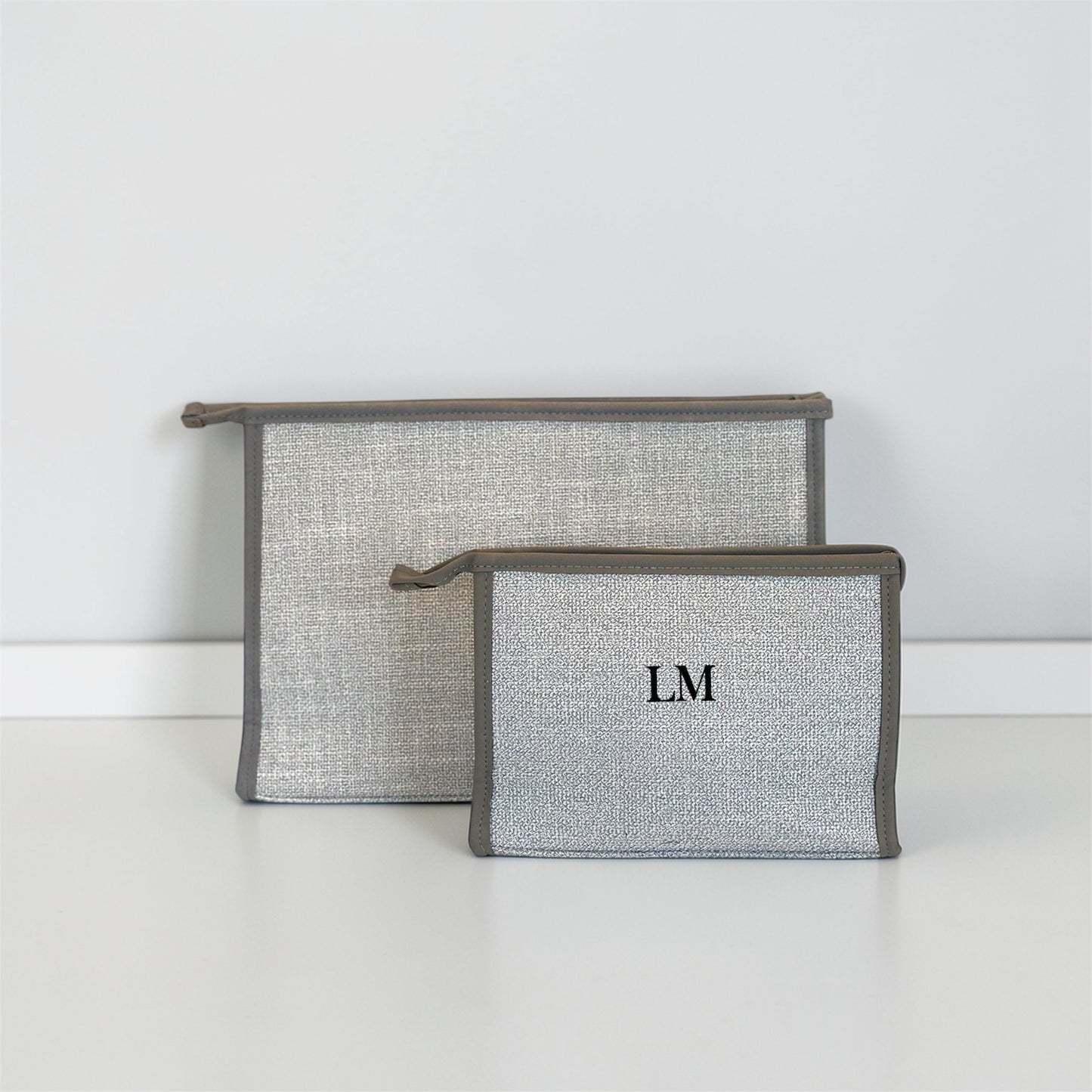 Two gray pouches with monogram initials on a white surface and background