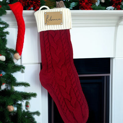 Red Christmas stocking with a white cuff on a fireplace mantle, decorated with greenery and a small tree.