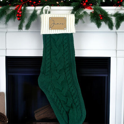 Green knitted Christmas stocking with 'James' tag hanging on a fireplace mantel.